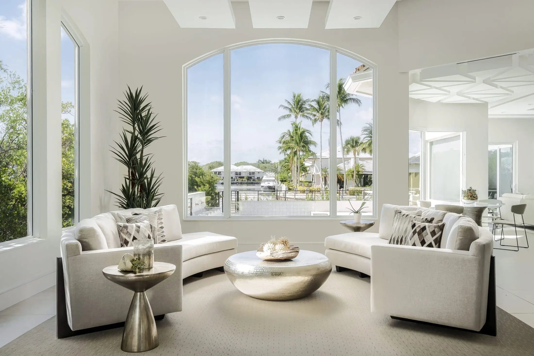 Boca Raton coastal living room with curved sofas, large arched window, and metallic coffee table overlooking the water.
