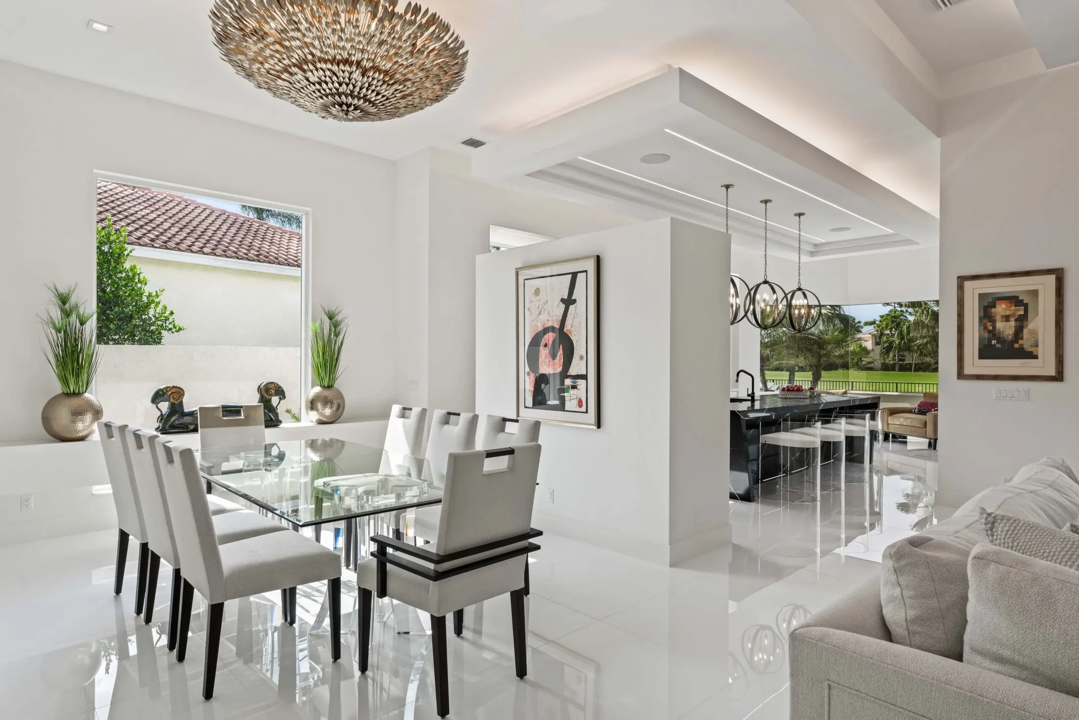 Contemporary dining room with a glass table, statement chandelier, and open view into the modern kitchen.