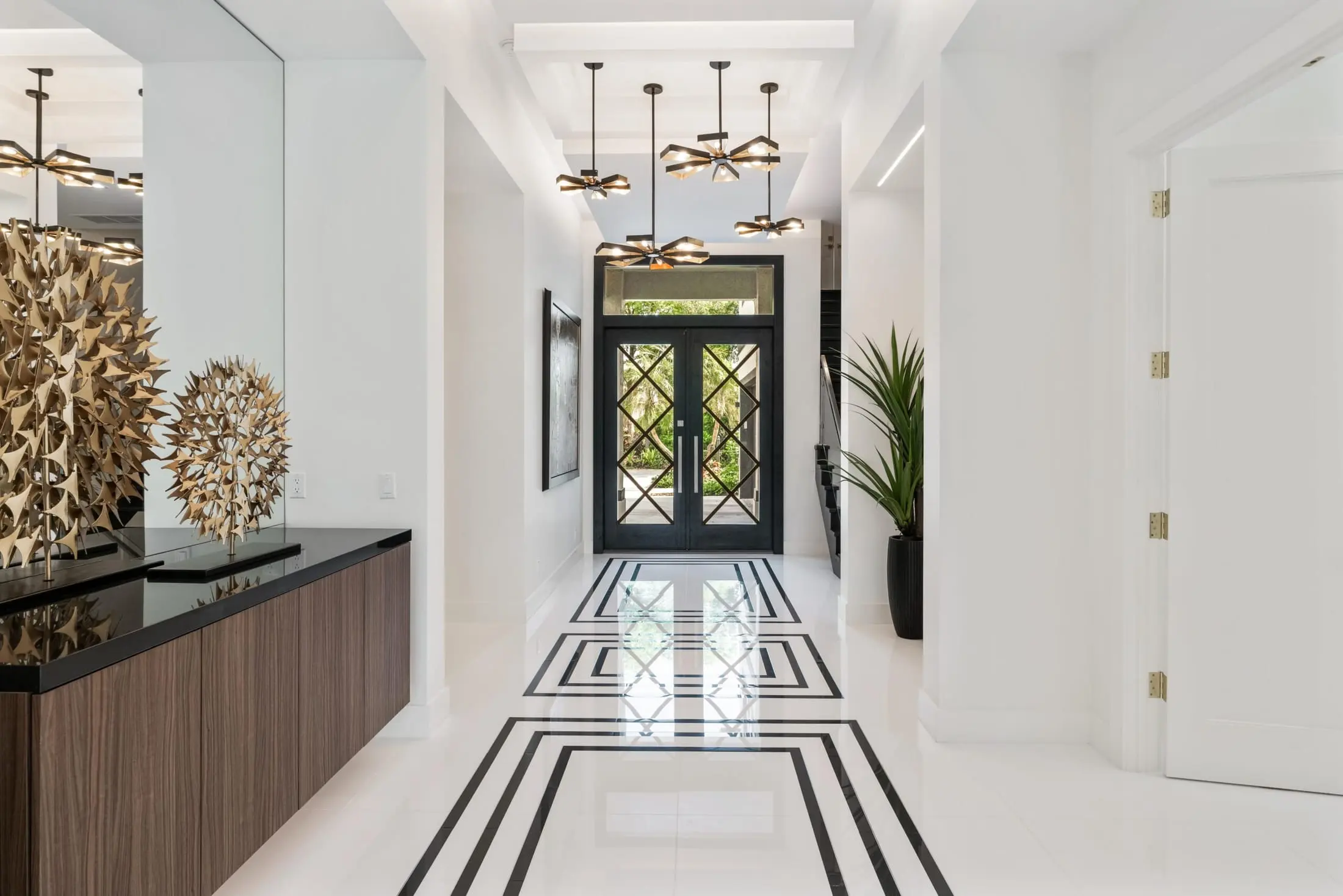 Modern foyer with geometric black-and-white tile floor, gold sculptural decor, and glass double door.