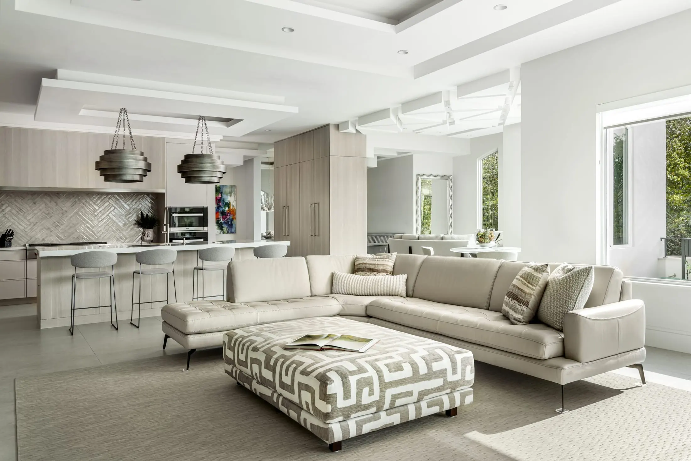 Bright open-concept Boca Raton living room and kitchen with neutral sectional sofa and patterned ottoman.