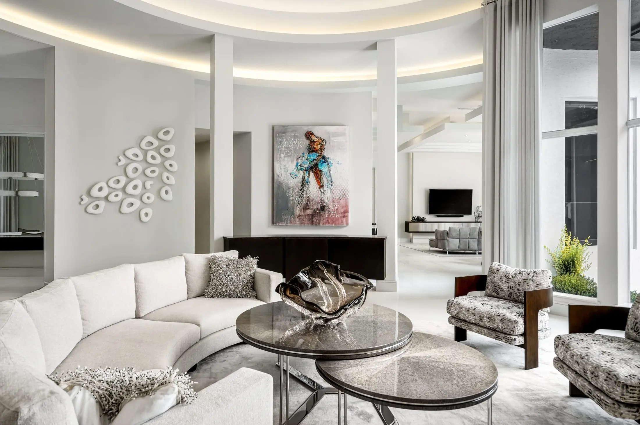 Modern living room with curved sectional sofa, marble coffee tables, and contemporary artwork.