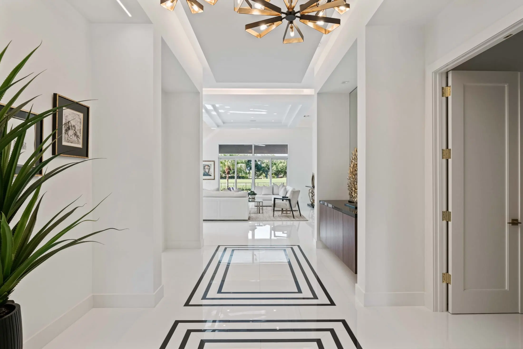 Modern hallway with geometric tile floor, gold light fixtures, and open view into bright living room.