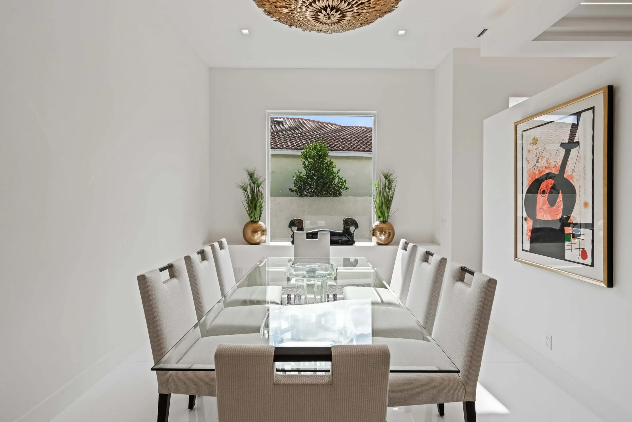 Modern dining room with a glass table, neutral upholstered chairs, and a sculptural chandelier centerpiece.