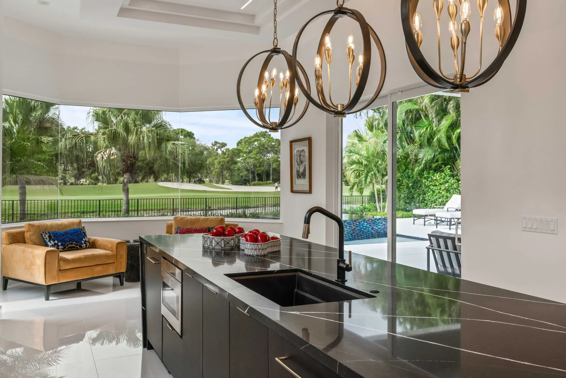 Delray Beach luxury kitchen design with black waterfall island, gold pendant lighting, and panoramic golf course and pool views.