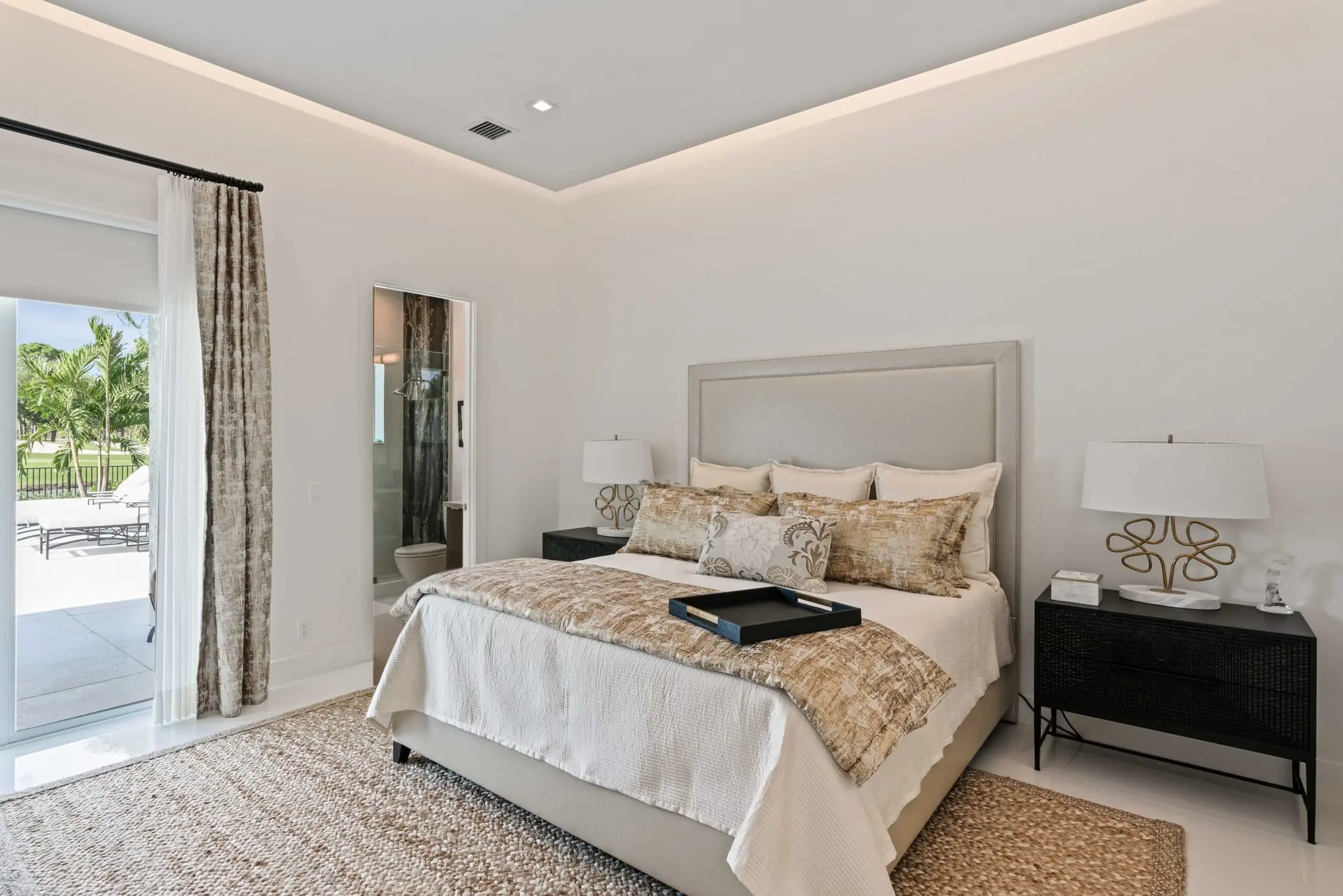 Elegant bedroom with neutral tones, textured bedding, and sliding doors opening to a tropical outdoor patio.