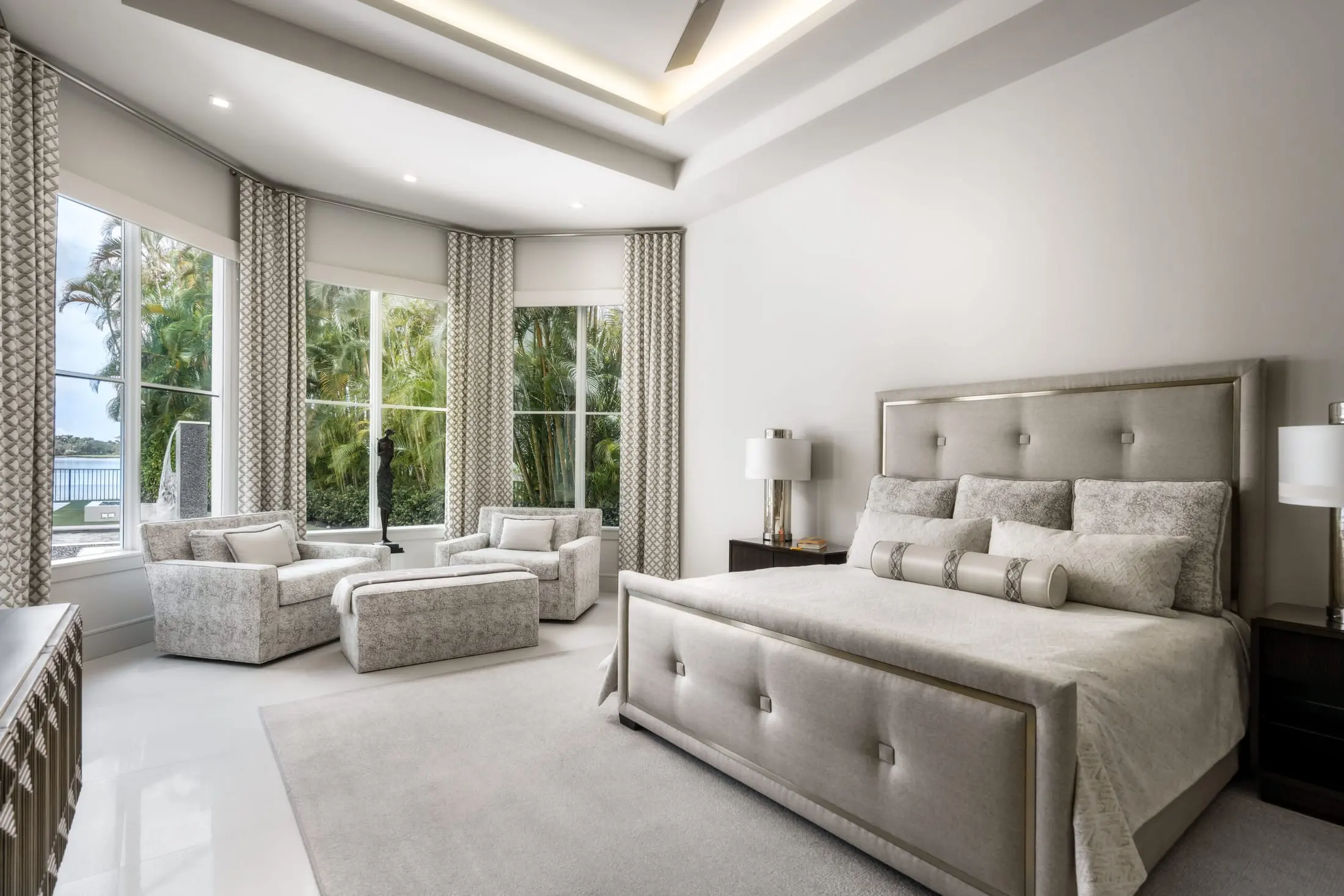 Primary bedroom with a tufted upholstered bed, soft neutral furnishings and tall windows.