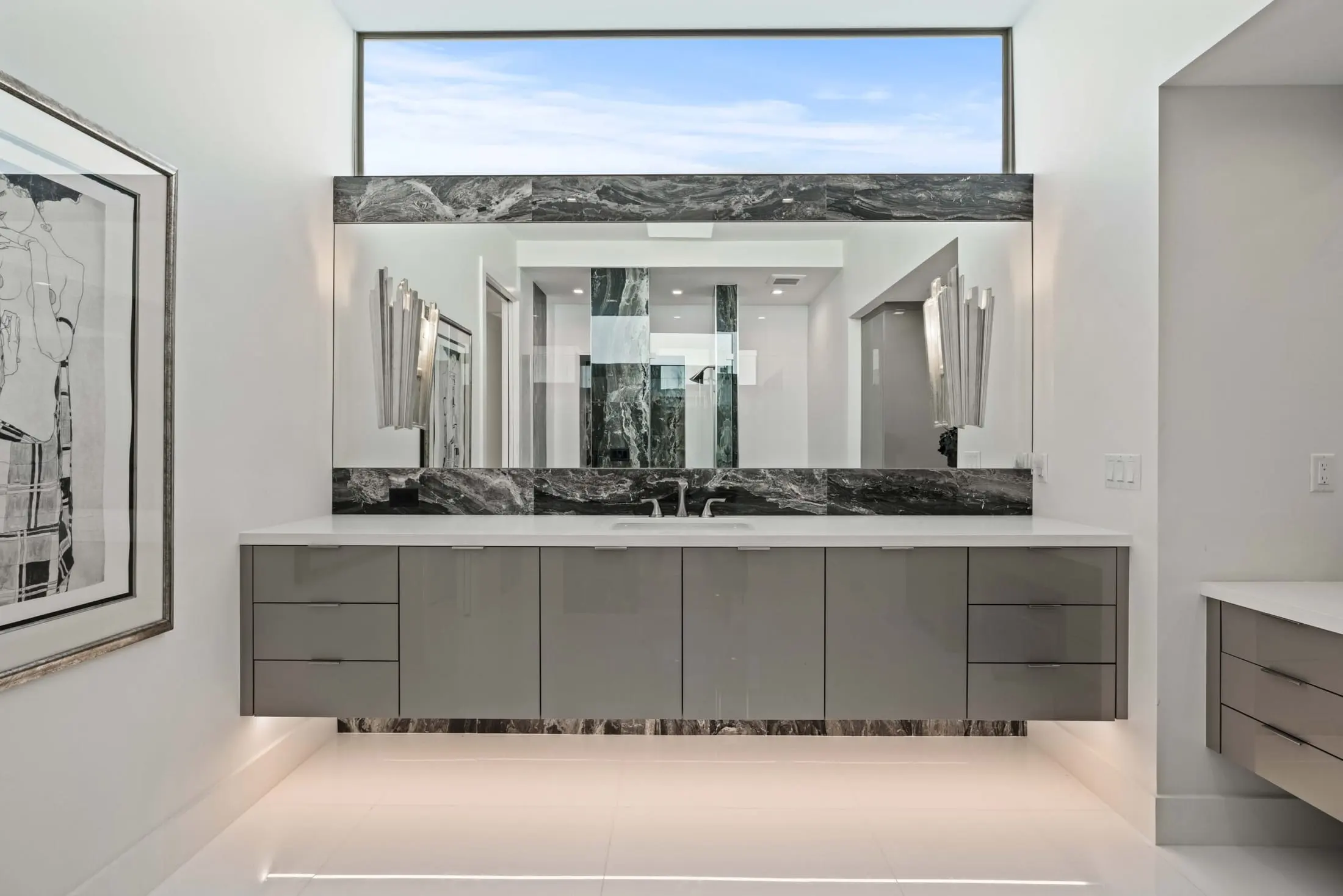 Contemporary bathroom with floating vanity, marble backsplash, and large mirror framed by natural light.