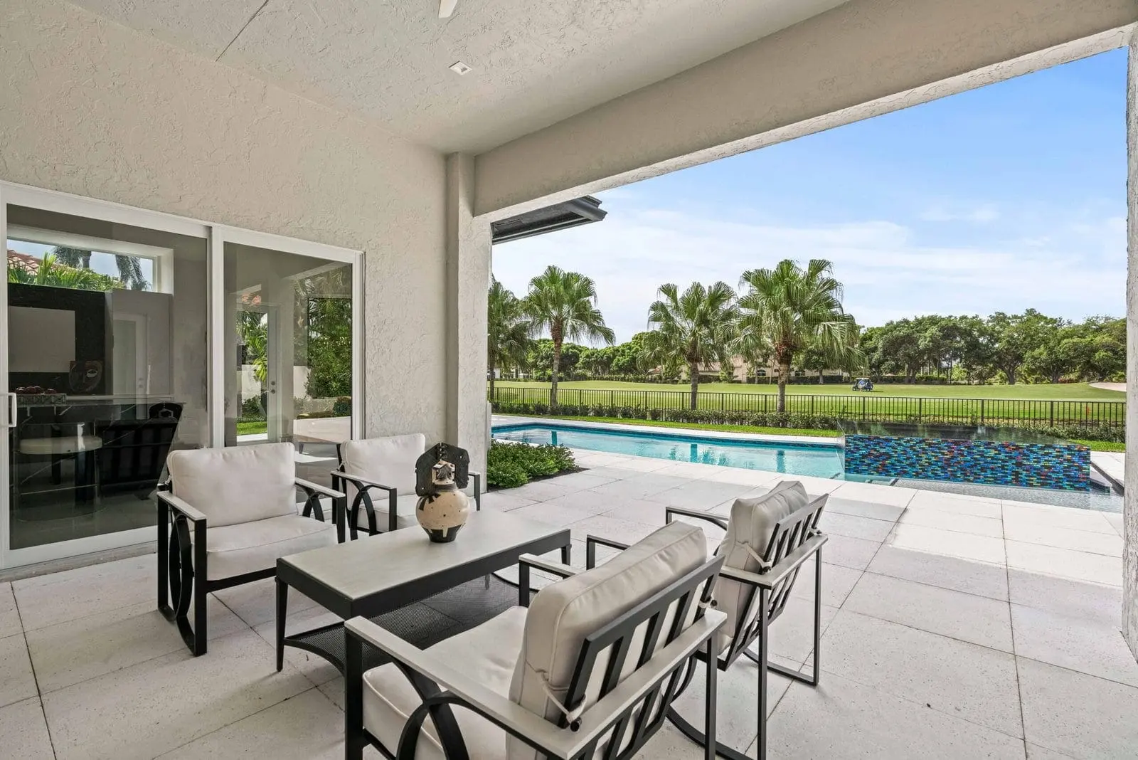 Covered patio with modern outdoor lounge seating overlooking a palm-lined lap pool in a Delray Beach luxury home.