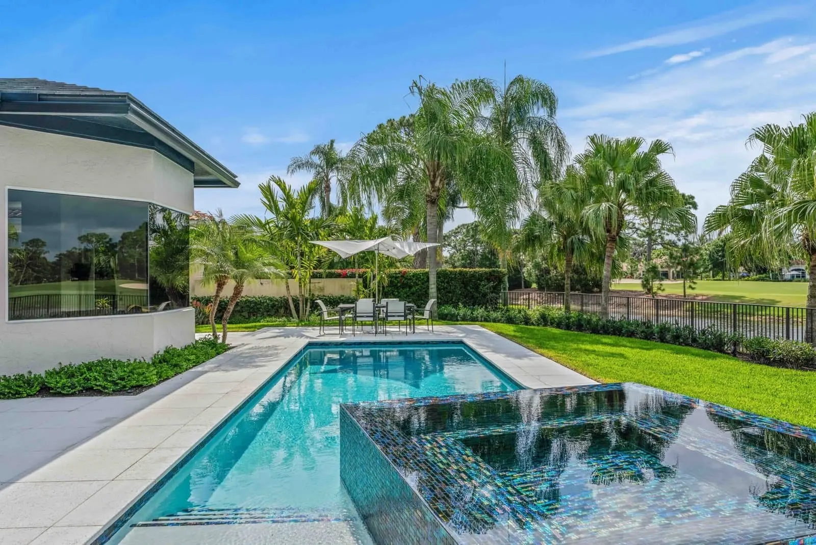 Modern pool with spa, lush landscaping, and a scenic golf course view in a Delray Beach luxury backyard.