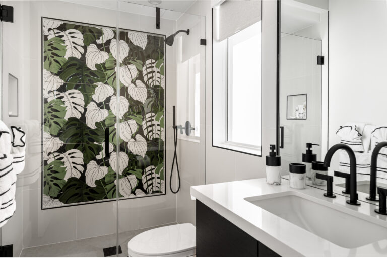 Modern bathroom with tropical leaf shower tile, black fixtures, and white quartz vanity.