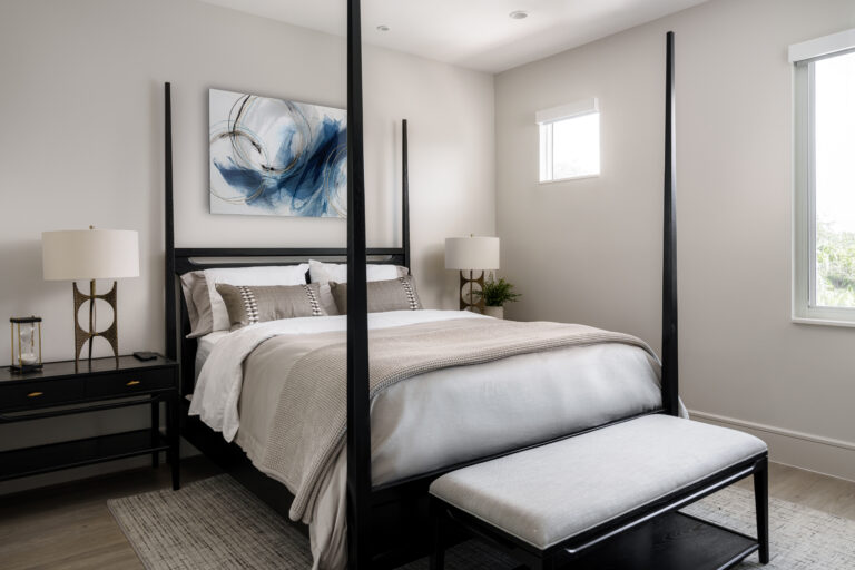 Modern bedroom with black four-poster bed, layered neutral bedding, and abstract blue wall art.