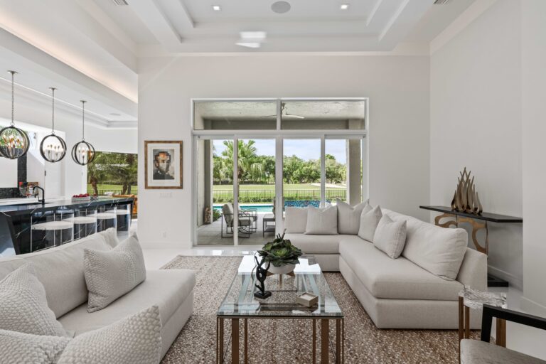 Delray Beach open-concept living room and kitchen with white sofas, marble island, and sliding doors leading to the pool.