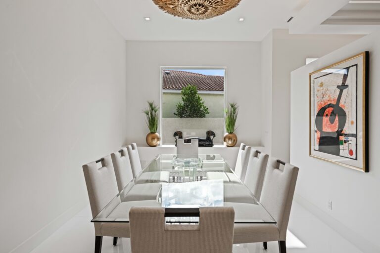 Modern dining room with a glass table, neutral upholstered chairs, and a sculptural chandelier centerpiece.