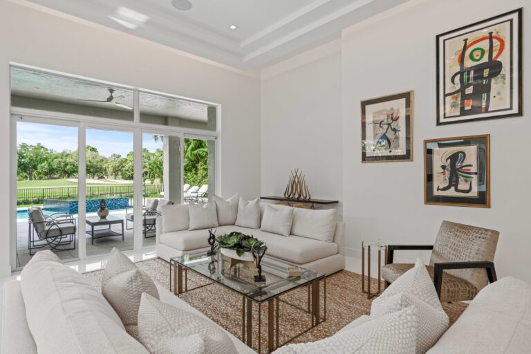 Elegant living room with white sectional sofas, glass coffee table, and modern art overlooking the pool.