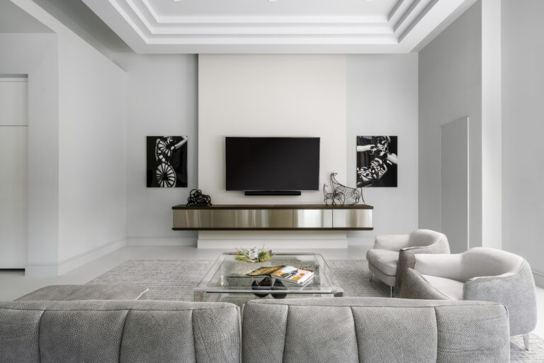 Contemporary living room with neutral furniture, wall-mounted TV, and modern black-and-white artwork.