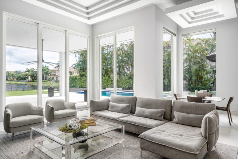 Bright modern living room with gray sectional sofa, glass coffee table, and poolside view by Integrative Designs Inc.