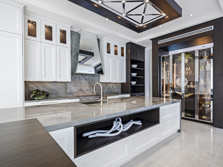 Palm Beach home modern luxury kitchen with marble countertops, mirrored range hood, glass display cabinetry, and dark wood accents.