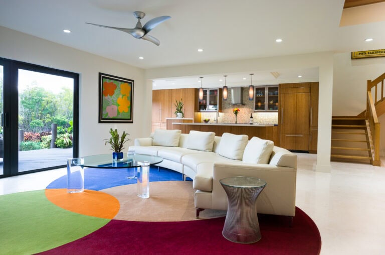 Vibrant South Florida living room with white sectional sofa, colorful geometric rug, and open kitchen design by Integrative Designs Inc.