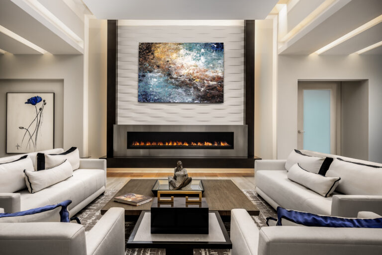 Contemporary living room in an Admiral’s Cove home in Jupiter featuring a modern linear fireplace, textured feature wall, abstract art, and white sofas with bold accents.