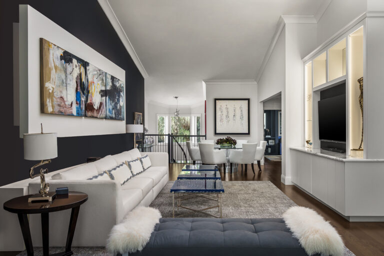 Modern living room in an Admiral’s Cove home in Jupiter with a white sofa, bold abstract art wall, custom built-in media cabinetry, and open dining area.